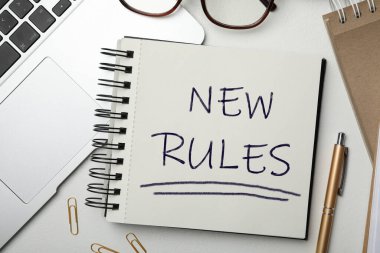 Not defterinde yeni kurallar, dizüstü bilgisayarlar ve kalemler beyaz masada, düz konum