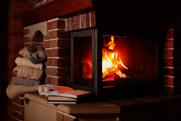 Stack of knitwear near fireplace with burning wood indoors. Winter vacation