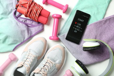 Beyaz arka planda fitness uygulaması ve spor aksesuarları olan akıllı telefon, düz uzanma