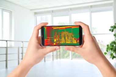 Bir kadın akıllı telefondan termal izleyici kullanarak odada ısı kaybı tespit etti. Enerji verimliliği