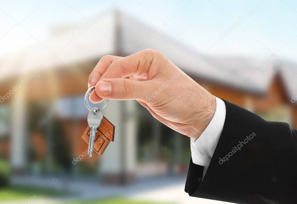 Man with key near new modern house outdoors, closeup
