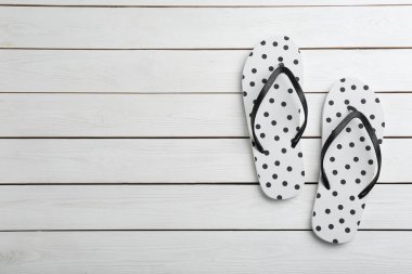 Beyaz ahşap arka planda şık parmak arası terlikler, düz yatış. Metin için boşluk