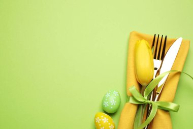 Yeşil arka planda çiçek dekoru olan çatal bıçak takımının üst görünümü, metin için boşluk. Paskalya kutlaması
