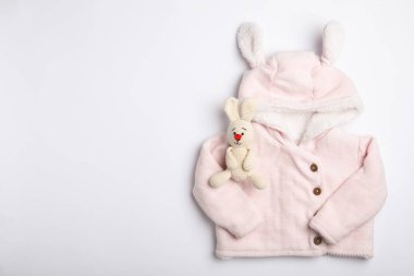 Beyaz arka planda çocuk kıyafetleri ve oyuncak tavşan manzarası.