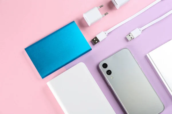 Mobile phone and portable chargers on color background, flat lay