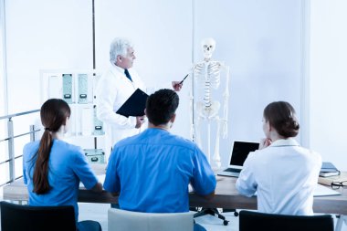 Tıp öğrencileri ve profesör sınıfta insan iskeleti anatomisi okuyor.