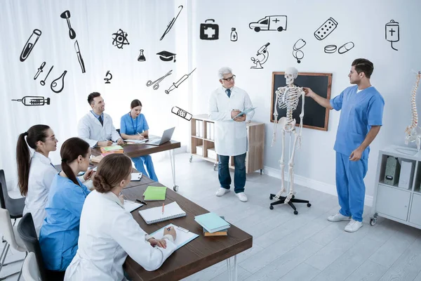 Medical students and professor studying human skeleton anatomy in classroom