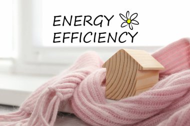 Enerji verimliliği kavramı. Pencere kenarındaki pembe eşarba sarılı ahşap ev modeli.