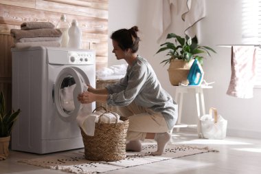 Çamaşır makinesinden çamaşırları çıkaran genç bir kadın.