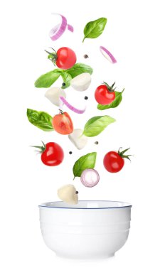 Mozzarella peyniri, domates, soğan ve fesleğen yaprakları beyaz arka planda kaseye düşüyor.