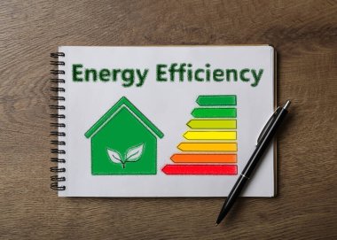 Enerji verimliliği kavramı. Çizilmiş ev ve çizelgeli defter ahşap masa, üst görünüm