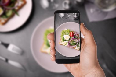 Blogcu masadaki jambonlu lezzetli sandviçin fotoğrafını çekiyor. Yemek fotoğrafçılığı