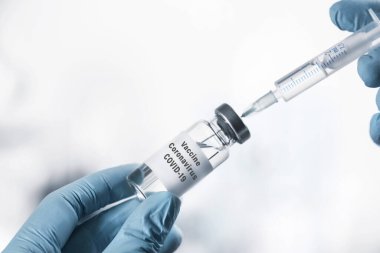 Doktor şırıngayı beyaz arka planda koronavirüs aşısıyla dolduruyor.
