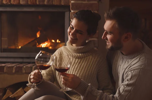 Lovely couple with glasses of wine near fireplace at home. Winter vacation