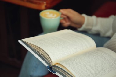 Elinde kahve fincanı olan kadın kitap okuyor, yakın plan.