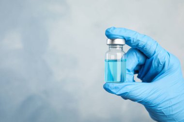 Doktor elinde açık mavi arka planda ilaç şişesi, yakın çekim görüntüsü ve metin için yer tutuyor. Aşılama ve aşılama