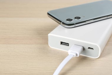 Cep telefonu ve portatif şarj aleti ahşap arka planda, yakın plan. Metin için boşluk
