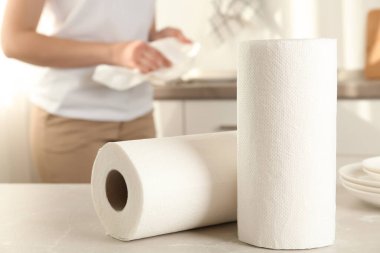 Kadın mutfakta havluyla tabak siliyor, kağıt rulolara odaklanıyor.