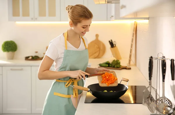 年轻女子在厨房的炉子上做饭 — 图库照片