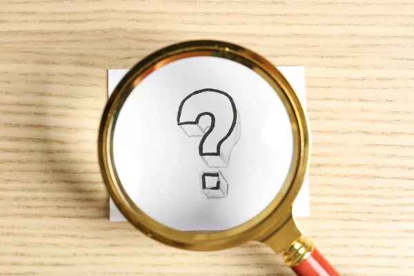Magnifying glass over card with question mark on wooden background, top view. Search concept