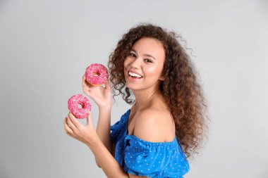 Açık gri arka planda donutları olan güzel bir Afro-Amerikalı kadın.