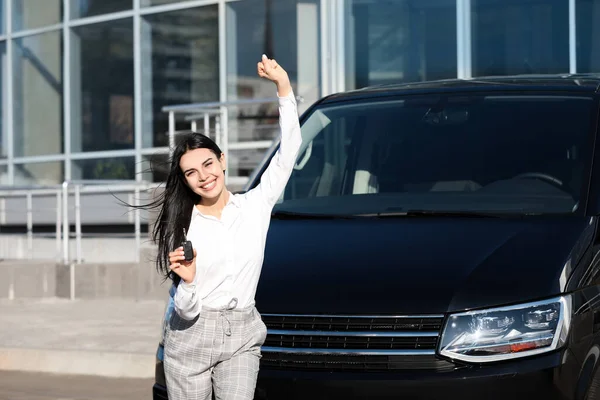 Young woman with key near car on city street. Buying new auto