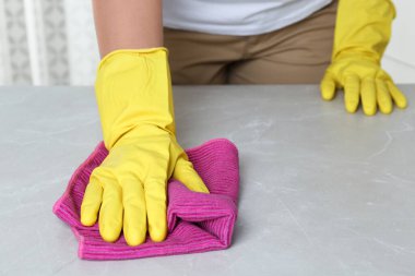 Eldivenli bir kadın, gri masayı kapalı bir şekilde temizliyor.