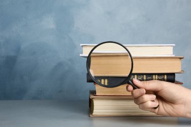 Gri masadaki antika kitap yığınının büyüteç camından bakan kadın, yakın plan. Arama konsepti
