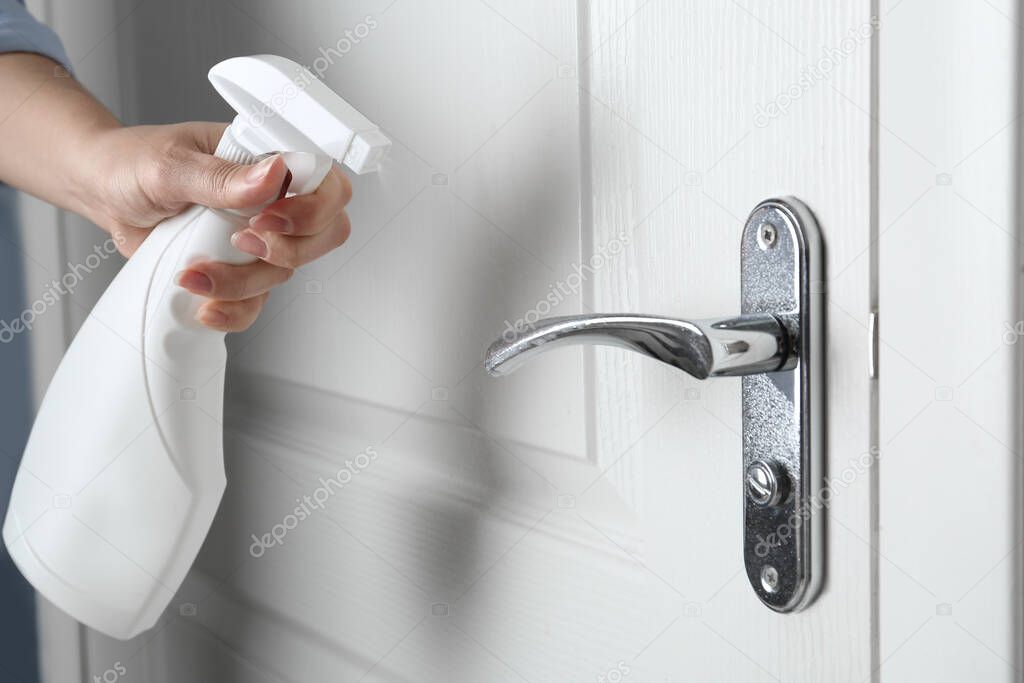 Woman spraying antiseptic onto door handle indoors, closeup