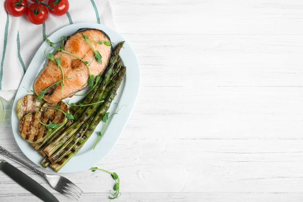 stock image Tasty salmon steak served with grilled asparagus on white wooden table, flat lay. Space for text