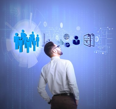 Ofisteki genç işadamı farklı simgelerle ve insan figürleriyle sanal ekrana bakıyor. Finans ticareti kavramı