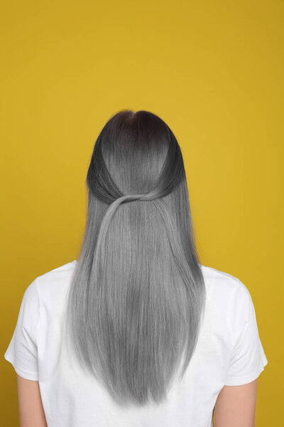 Woman with gray hair on yellow background, back view