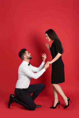 Nişan yüzüklü bir adam kırmızı arka planda kız arkadaşına evlenme teklif ediyor.