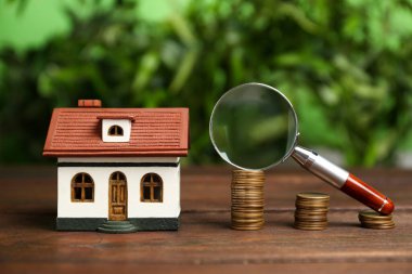 Ev modeli, bozuk paralar ve büyüteçler arka planda bulanık duran ahşap masa üzerinde. Arama konsepti