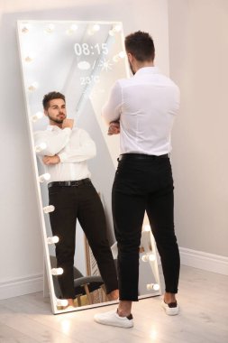 Genç adam evinde kendine akıllı aynada bakıyor.