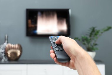 Televizyonda uzaktan kumandayla kanal değiştiren bir adam