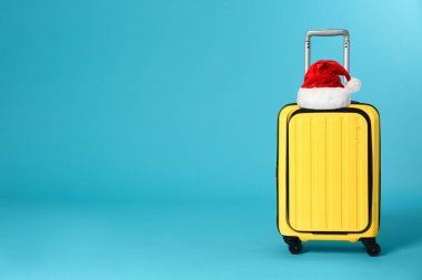 Mavi arka planda Noel Baba şapkası olan şık bir bavul. Mesaj için yer var. Noel tatili  