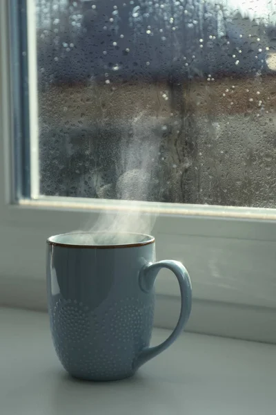 Cup of hot drink near window on rainy day