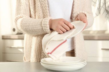 Mutfakta açık gri masada havluyla tabağı silen kadın, yakın plan.