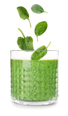 Taze yeşil ıspanak yaprakları beyaz arka planda smoothie ile cama dökülüyor.