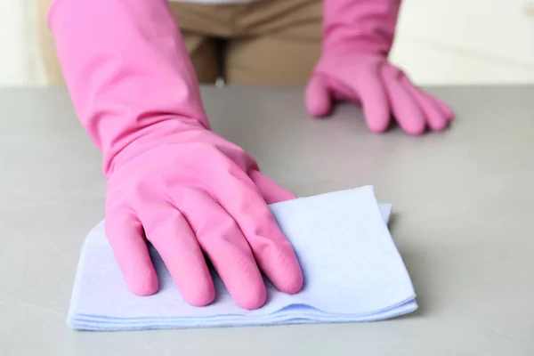 Woman in gloves wiping grey table with rag indoors, closeup