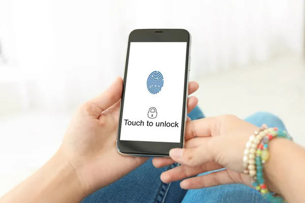 Woman holding smartphone with fingerprint sensor indoors, closeup. Digital identity