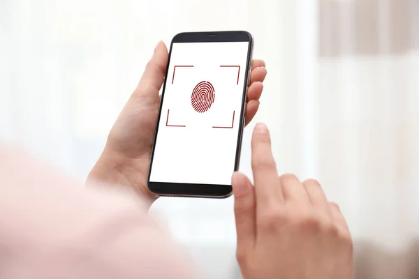 Woman holding smartphone with fingerprint sensor indoors, closeup. Digital identity