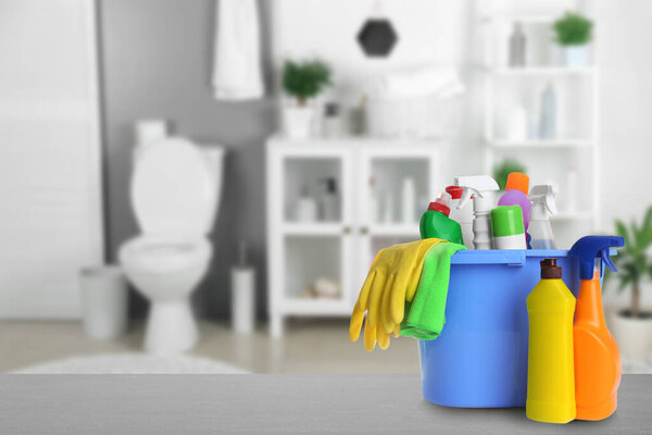 Ведро с чистящими средствами на сером каменном столе в ванной комнате, место для текста
