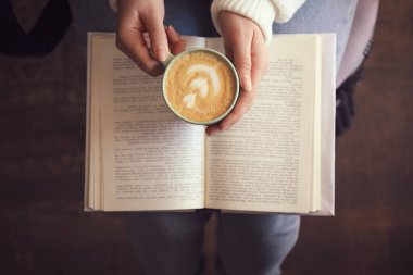 Bir fincan kahve içip kitap okuyan bir kadın.