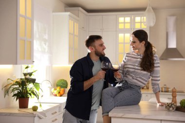 Birlikte mutfakta yemek pişirirken şarap içen genç ve güzel bir çift.