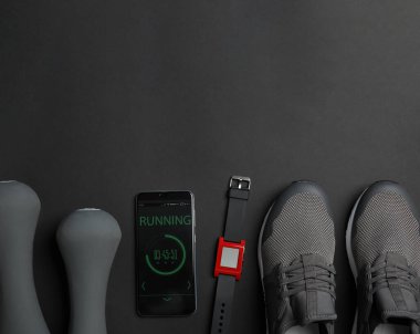 Siyah arka planda fitness ekipmanı ve akıllı telefondan oluşan düz bir kompozisyon. Metin için boşluk