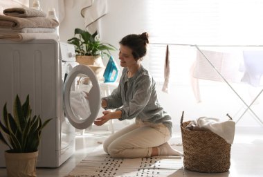 Çamaşır makinesinden çamaşırları çıkaran genç bir kadın.