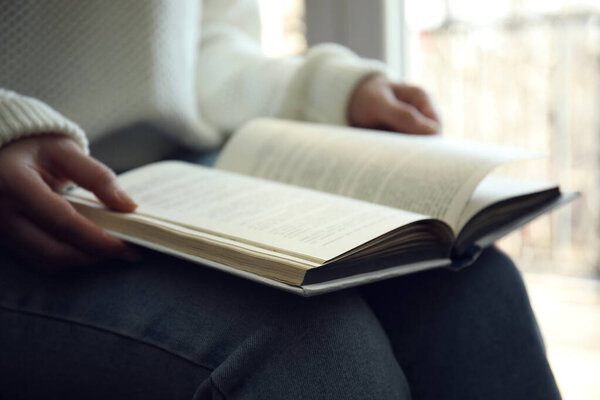 Женщина читает книгу у окна, крупным планом
