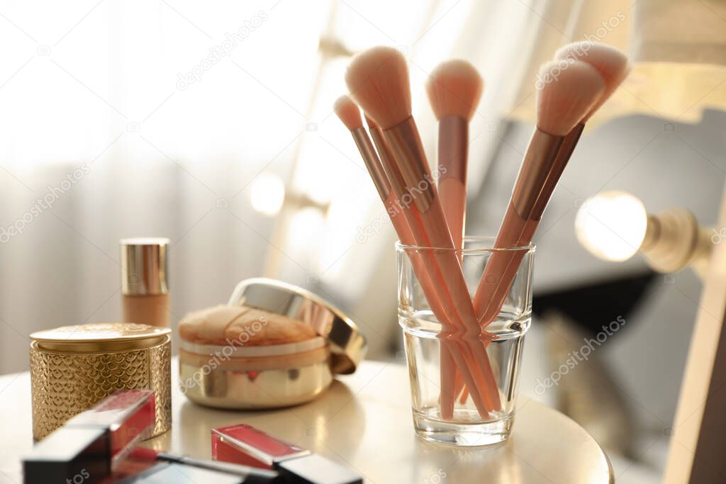 Makeup products and set of cosmetic brushes on table indoors. Interior element